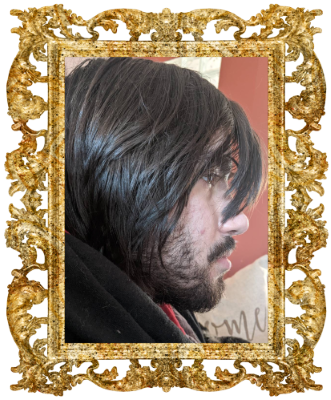 Hogg's boyfriend, man in his mid 20s with long dark hair and a short beard, photo is surrounded by an elabourate gold frame